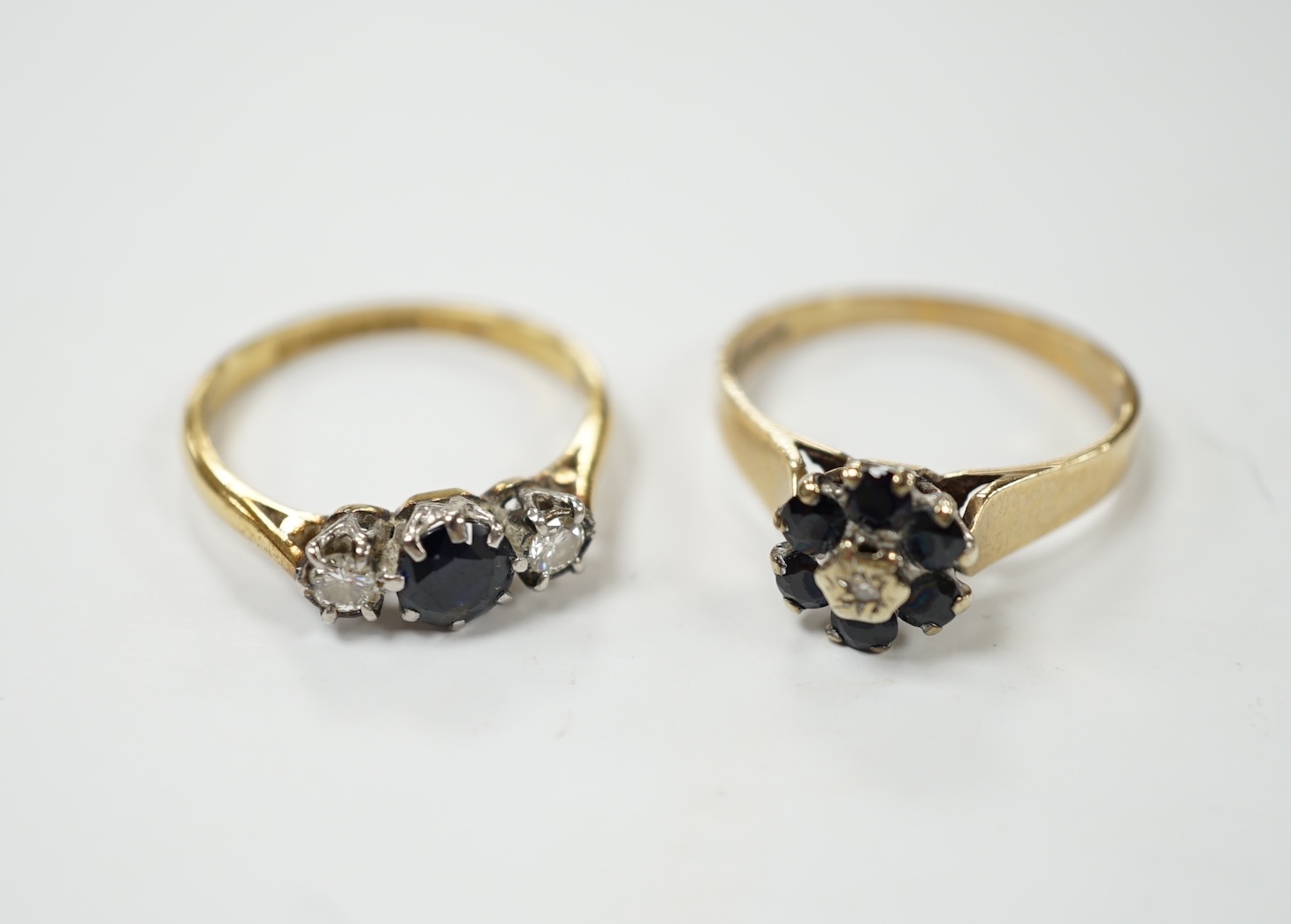 A modern 18ct gold, sapphire and diamond set three stone ring, size O, together with a similar 9ct gold, sapphire and diamond cluster set ring. Condition - fair